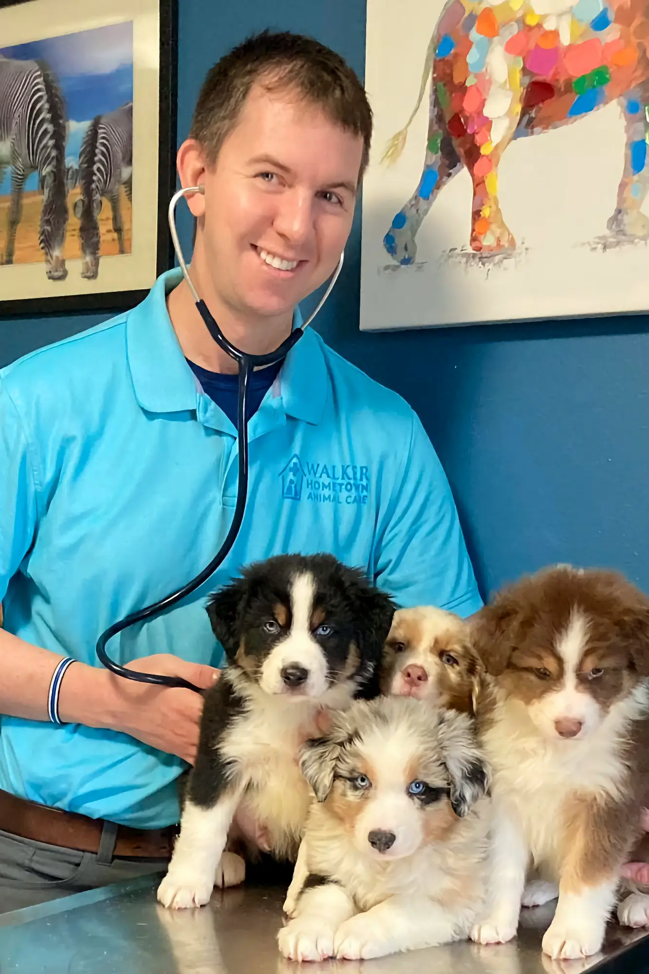 Dr. Walker wearing a blue shirt smiling for the camera with four puppies.